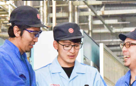 作業服を着た男性社員3名が談笑している写真